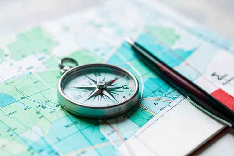 Uma bússola sobre um mapa, simbolizando a escolha de um caminho profissional, com uma caneta e um caderno ao lado.