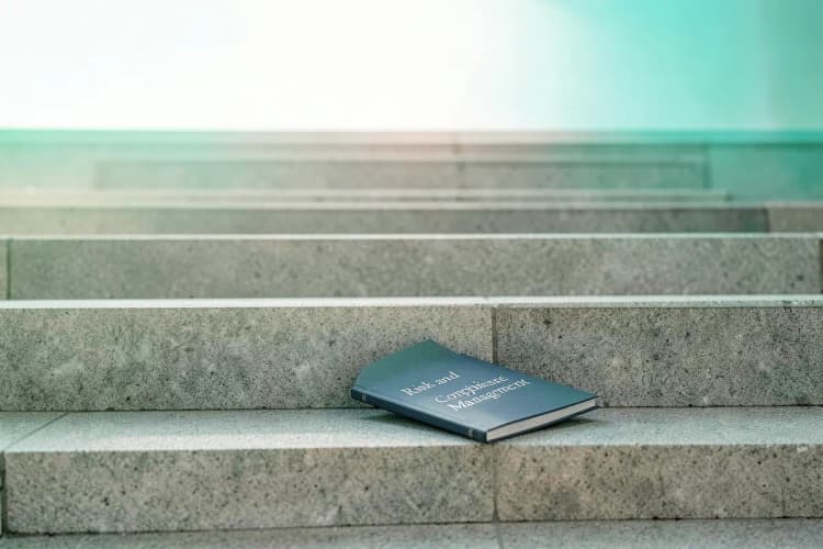 Um caminho de degraus levando a um horizonte iluminado, com um livro aberto sobre gestão de risco e compliance em primeiro plano, simbolizando os próximos passos na carreira.