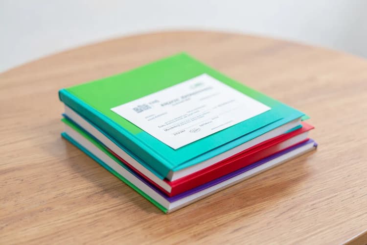 Uma pilha de livros sobre um balcão de madeira, com um certificado parcialmente visível no topo.